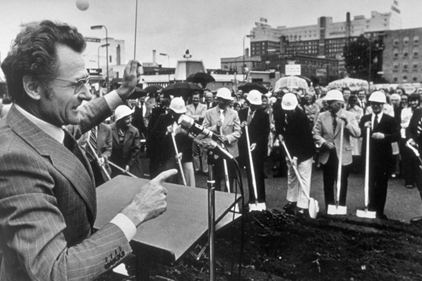 Stanislaw Skrowaczewski talking at a podium at a construction site to a group of people