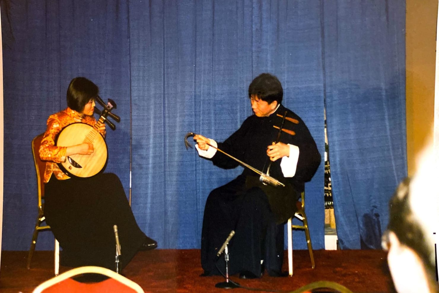 Mei Hu, left, and Zhengang Xie, right, perform together seated in front of a blue curtain