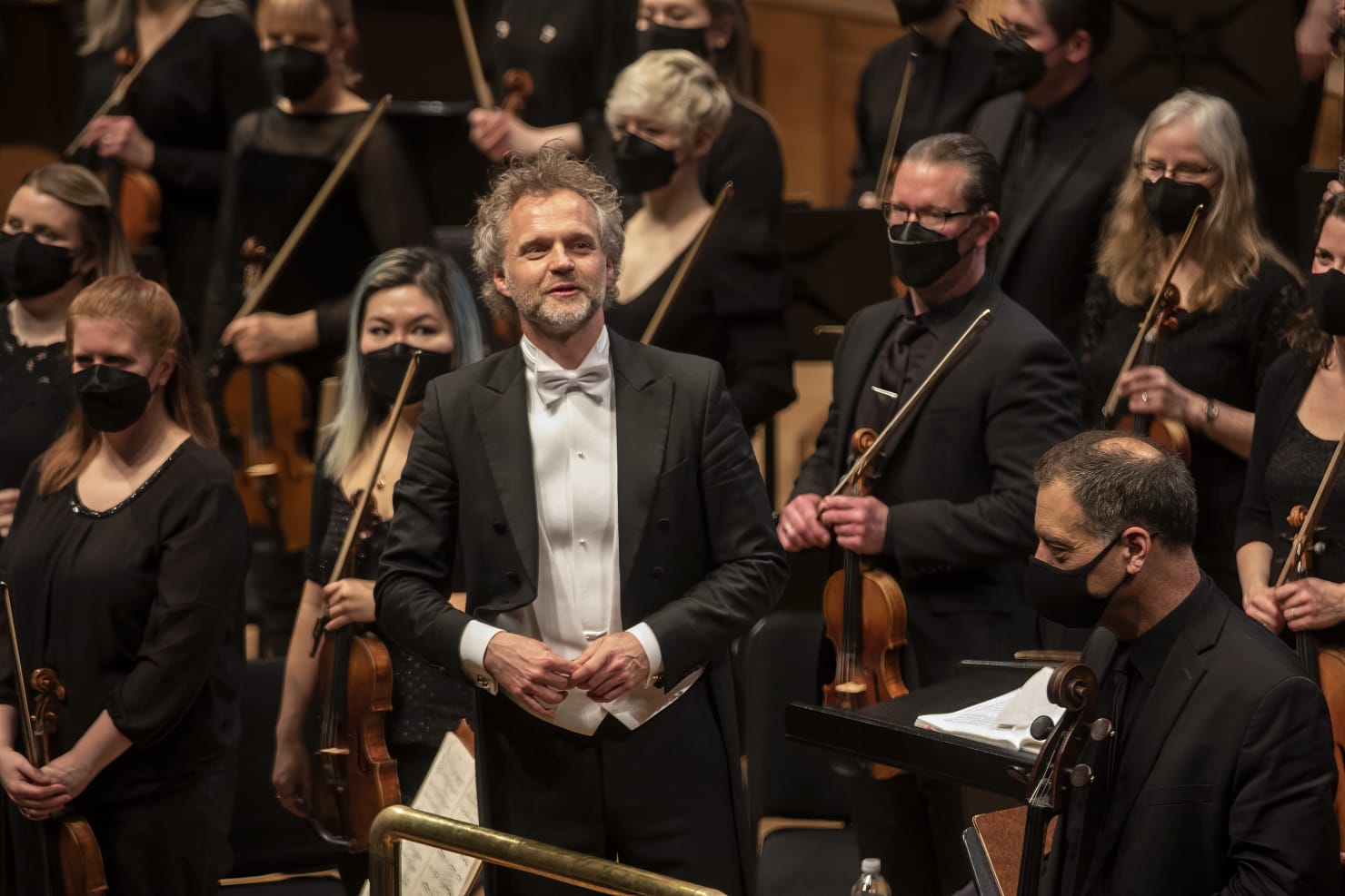 Thomas Søndergård standing at the podium for an applause; the Orchestra is standing behind him.