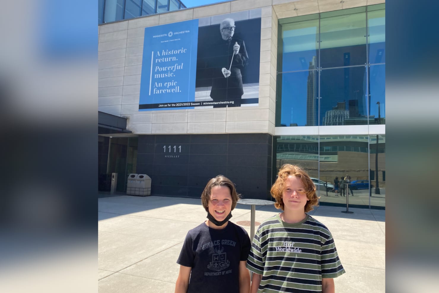 Whitsun (12) and Morrow (13) stand in front of Orchestra Hall in Minneapolis. A large photo of Osmo Vänskä is shown on the wall of the building behind them. 