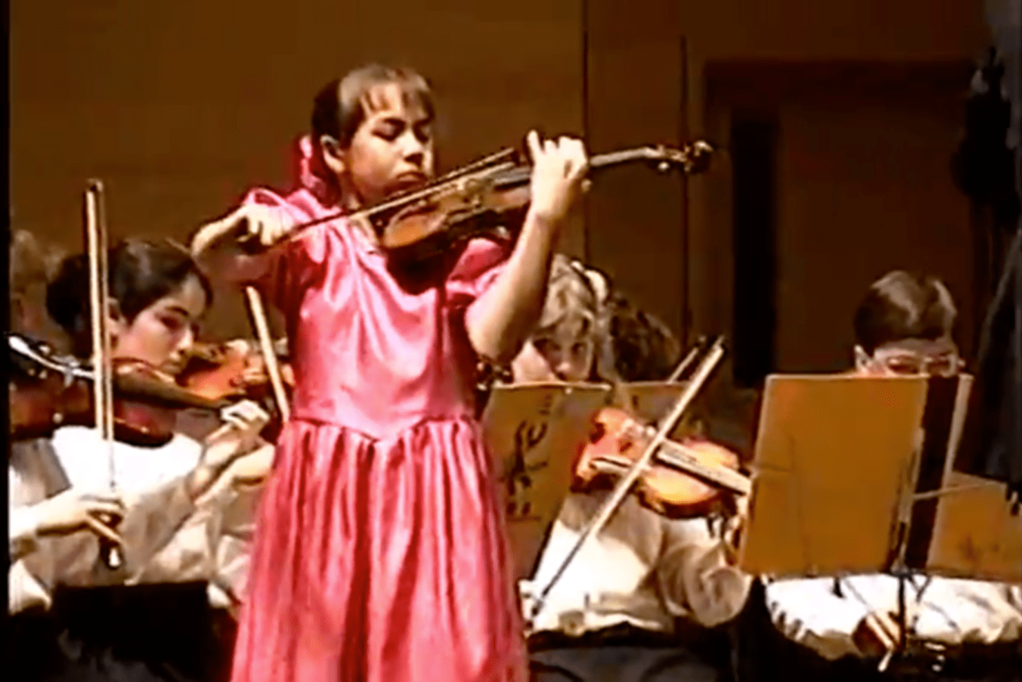 A 10-year-old Ariana Kim plays violin in front of youth orchestra in a pink dress