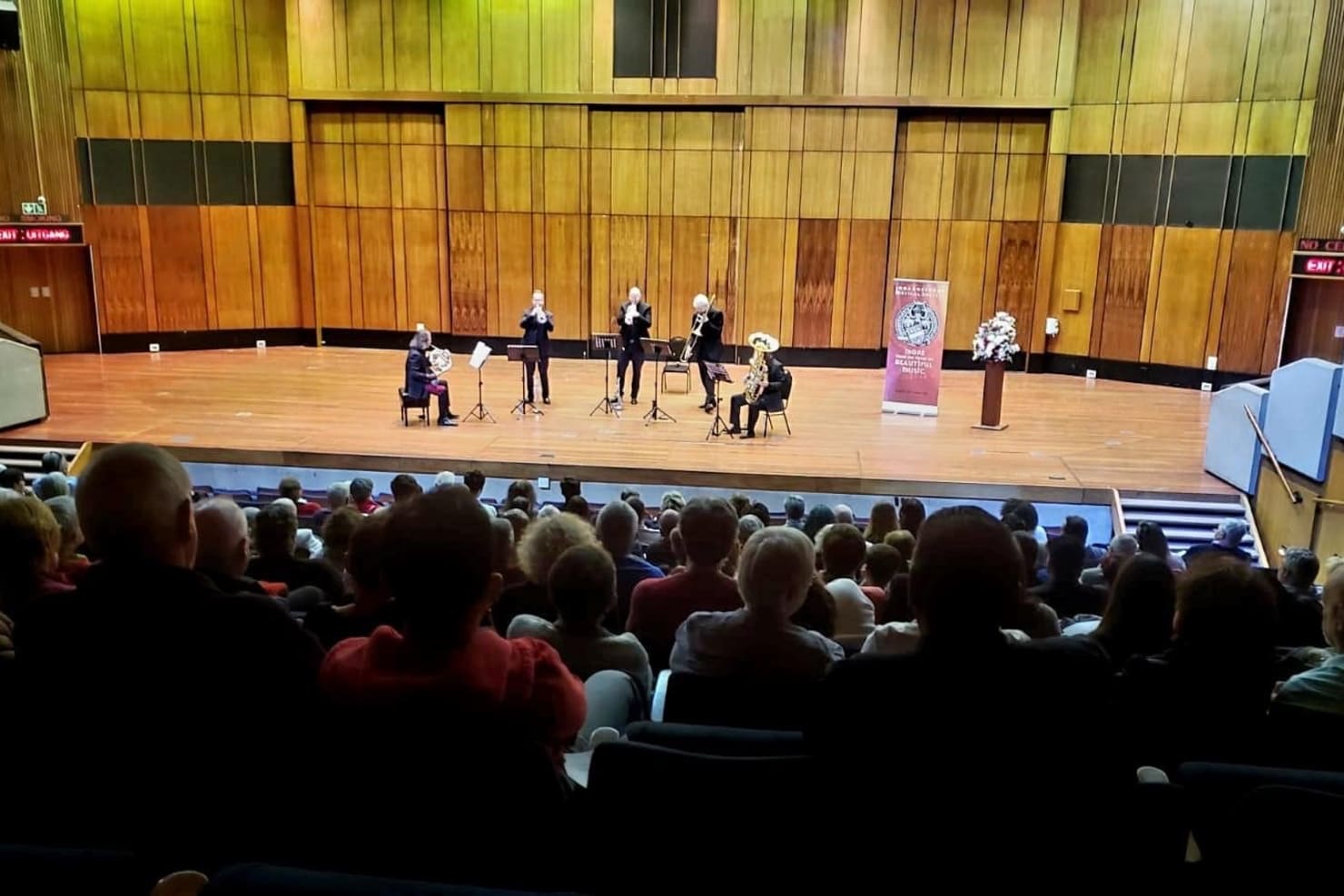 Viewed from the back of the concert hall, five brass players from the Minnesota Orchestra performing at Linder Auditorium at the University of the Witwatersrand in Johannesburg.