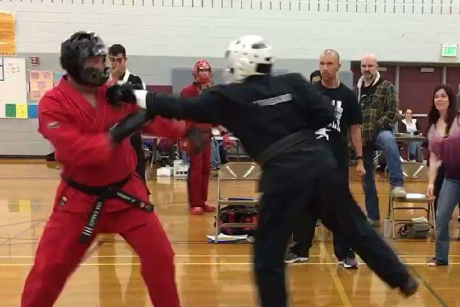 Two men sparring in a gym, wearing robes and protective gear. One is dressed in red, the other in black.