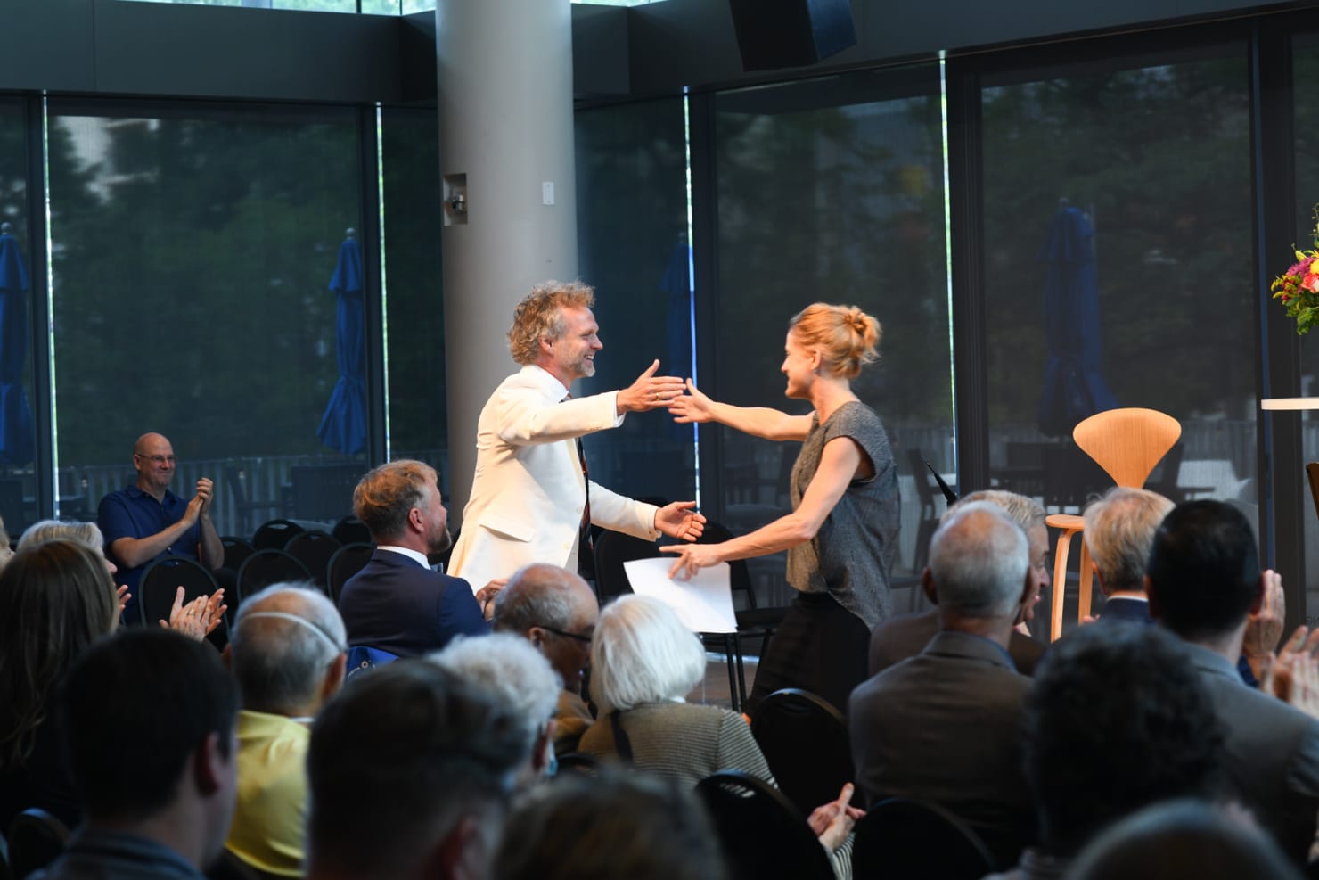 An audience is seen clapping while, before them Kristen Bruya and Thomas Sondergard give one another a hug.