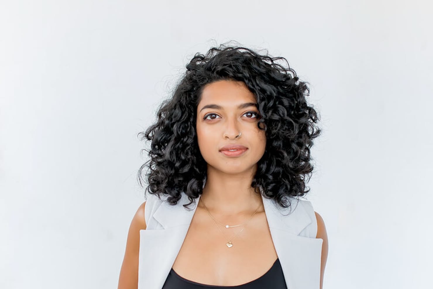 An image of a woman, Chelsea de Souza, standing before a white background and looking directly at the camera, hands in her pockets.
