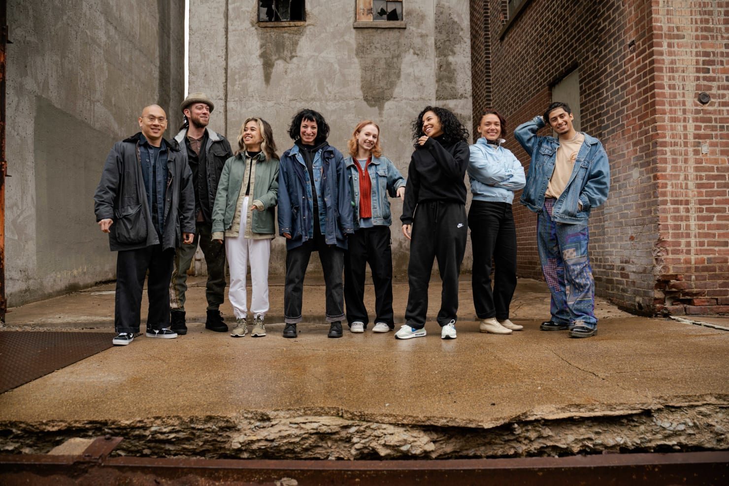 An image of eight people standing casually in an industrial area, smiling and laughing.