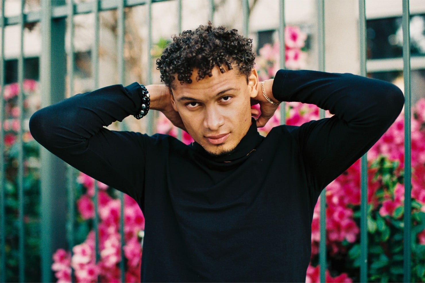 Manzari wearing a dark turtleneck, standing outside before a flowering bush.