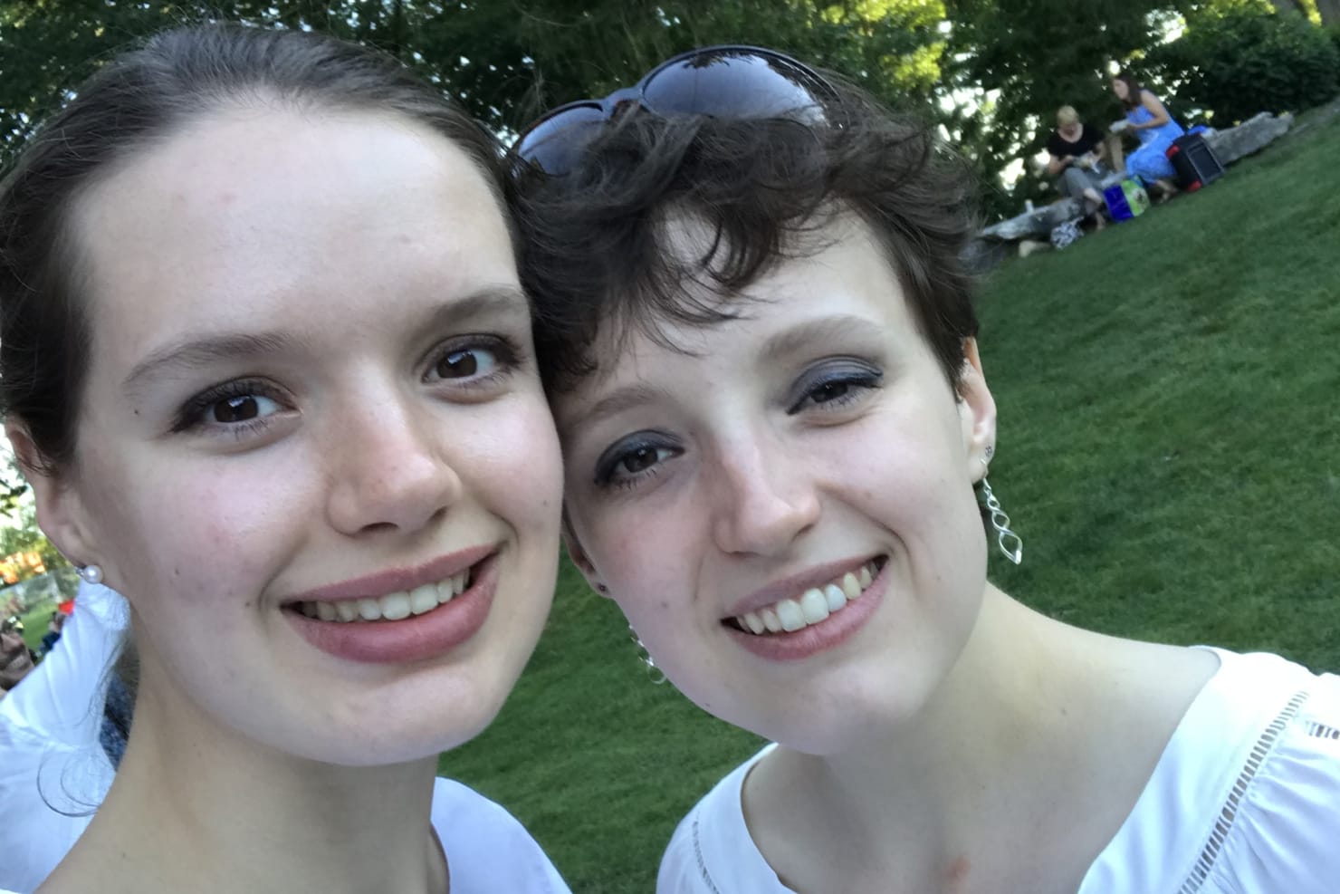 Two women--Emily and Sarah--posing in front of the camera, dressed in white and in a park.