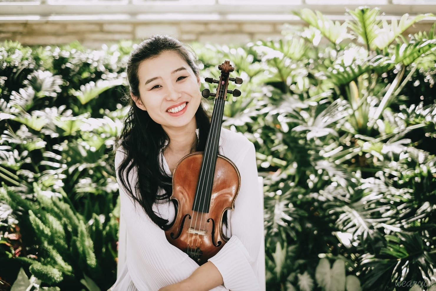 A portrait of Yi, holding her violin and smiling.