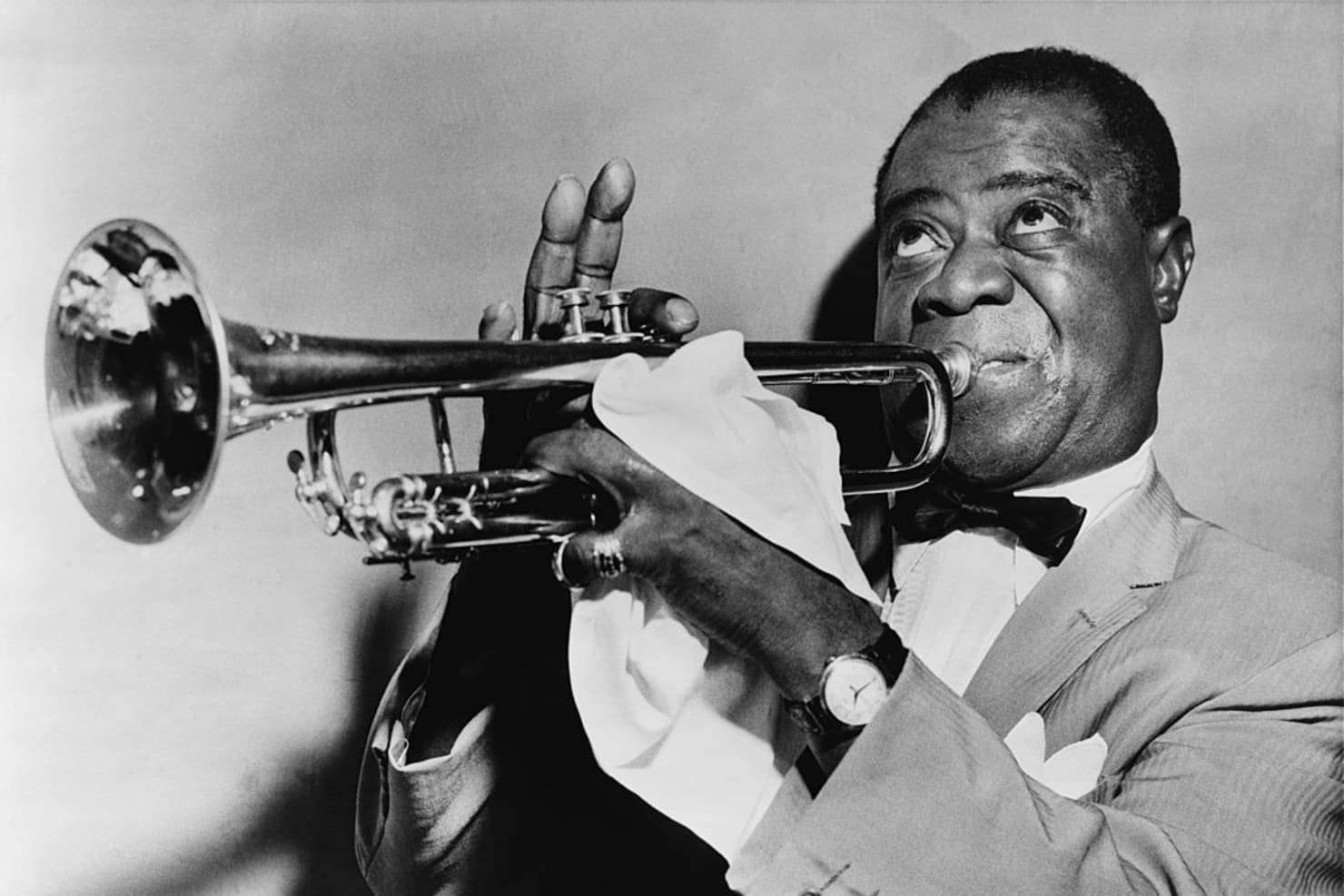 An image of trumpeter Louis Armstrong, wearing a suit and playing his instrument.