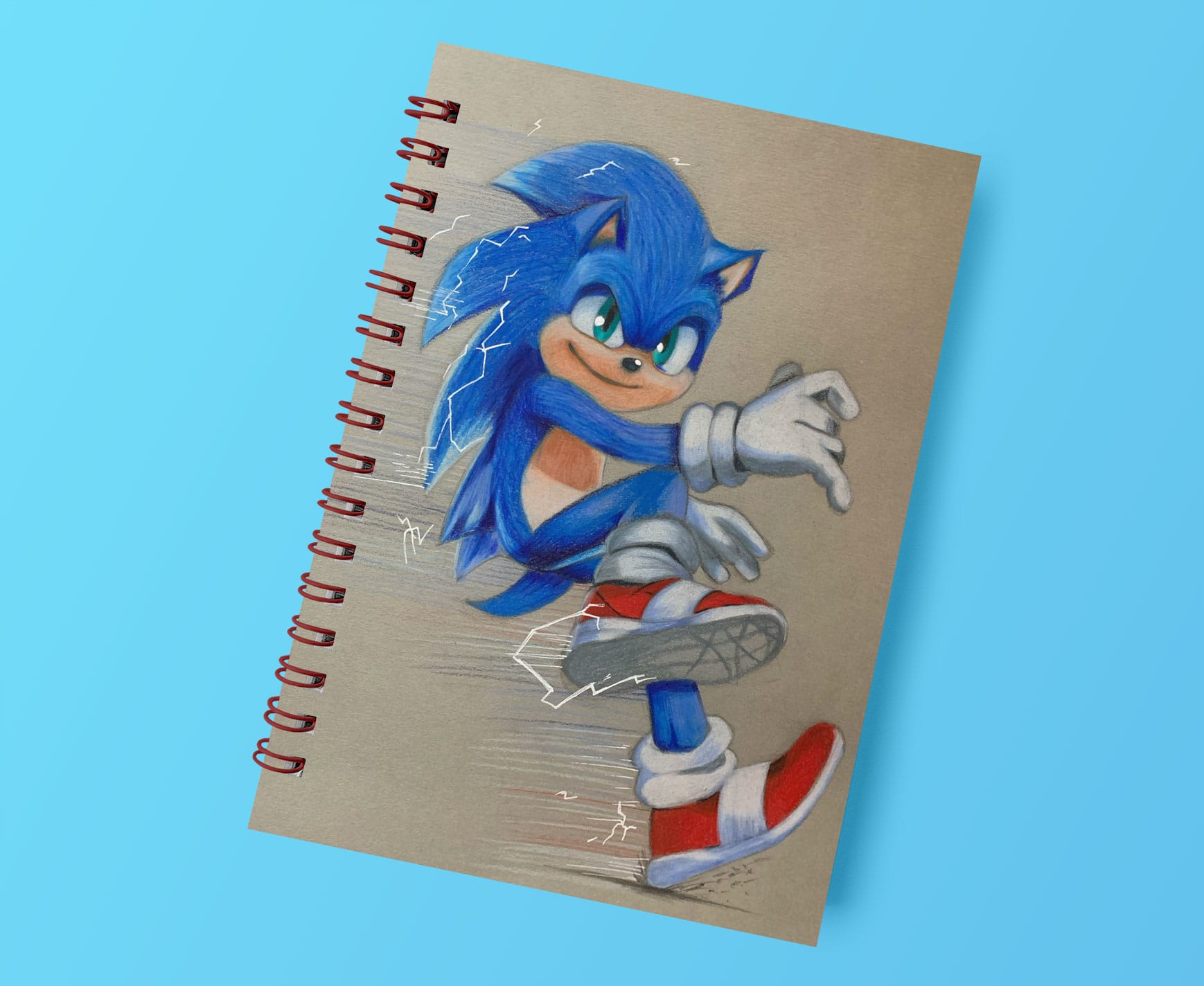 a drawing of sonic on grey paper shown on a ring bound sketchbook coloured with coloured pencils