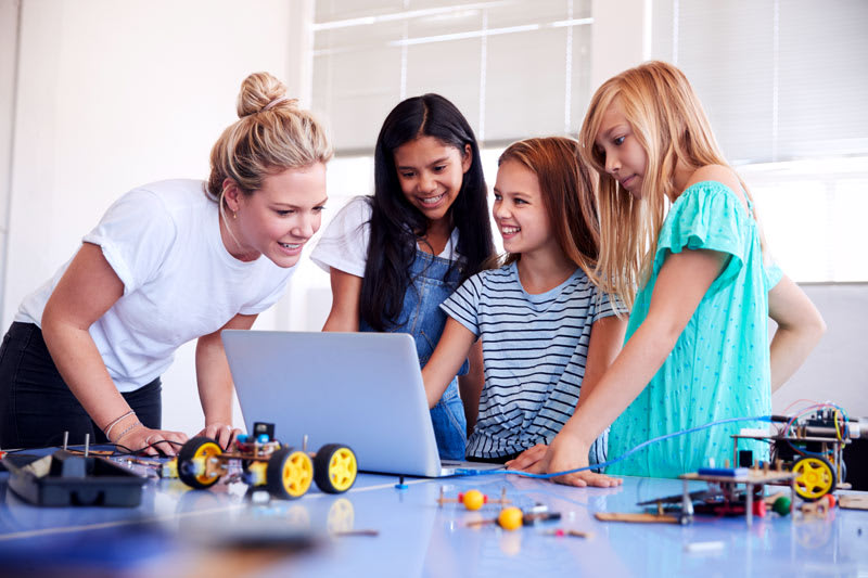 Teacher encouraging a group to work through a problem on a laptop