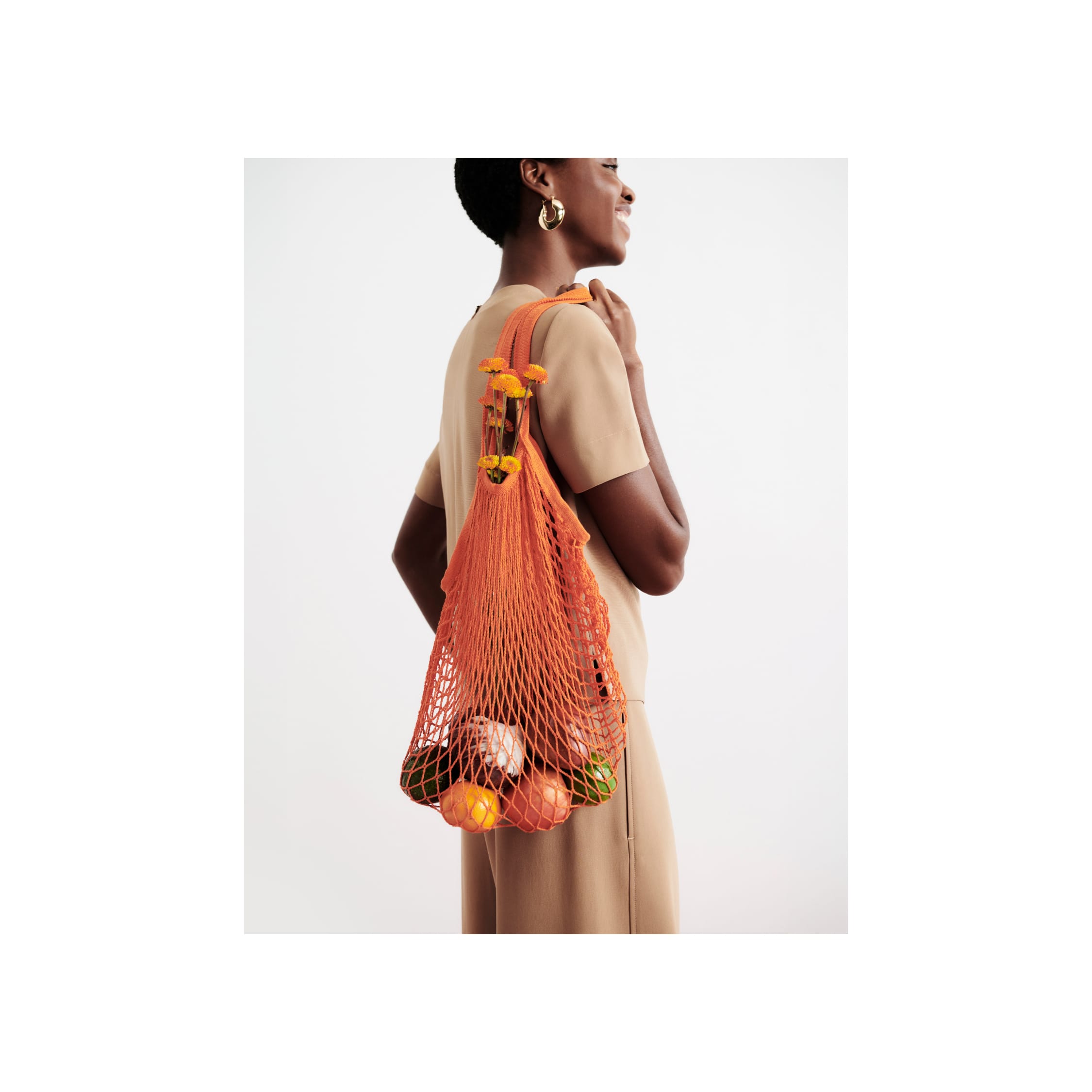 woman wearing light saddle short-sleeve Annika top and carrying orange bag of fruit over her shoulder