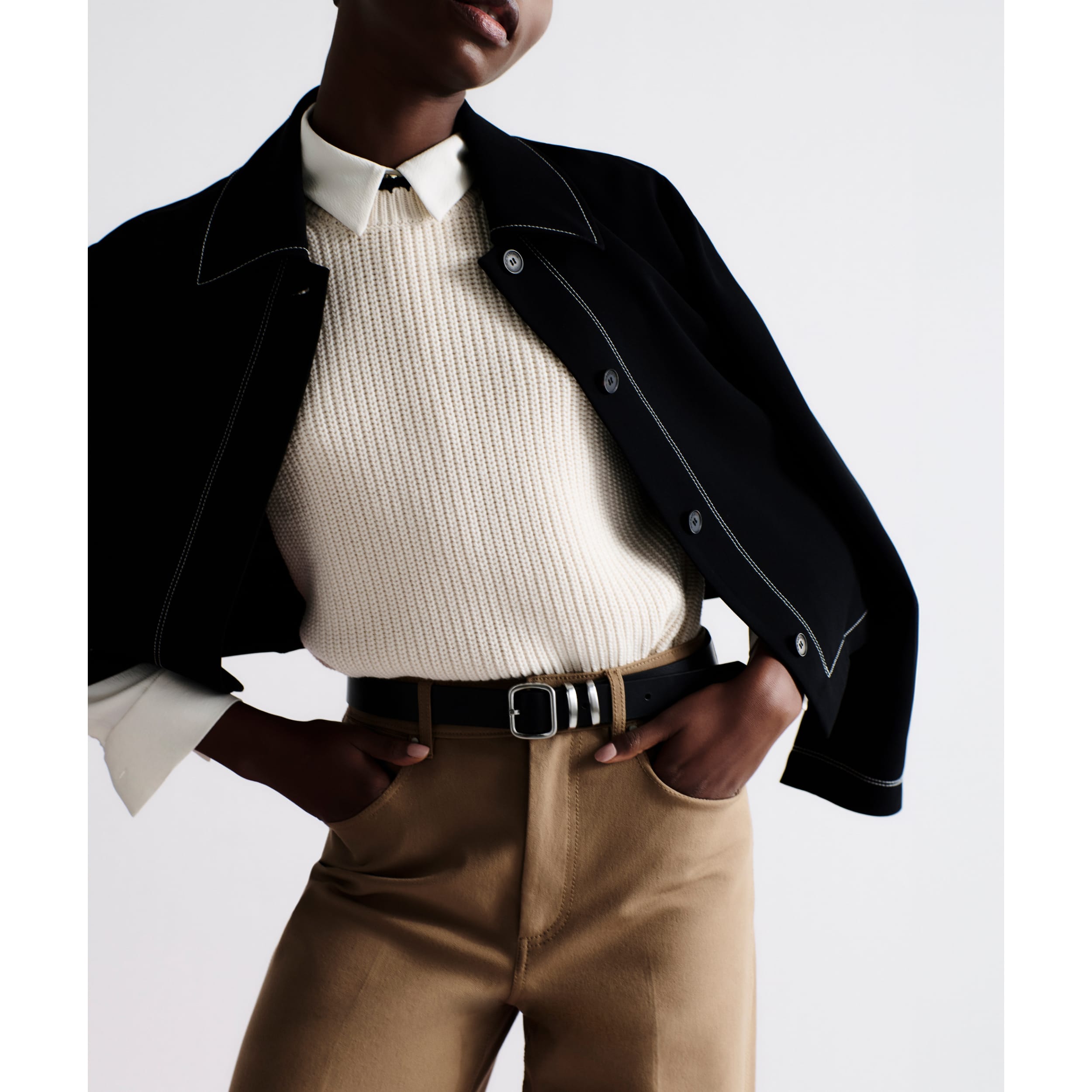 woman wearing white button-up shirt under white knit Giada sleeveless top with black contrast stitching with black jacket draped over her shoulders
