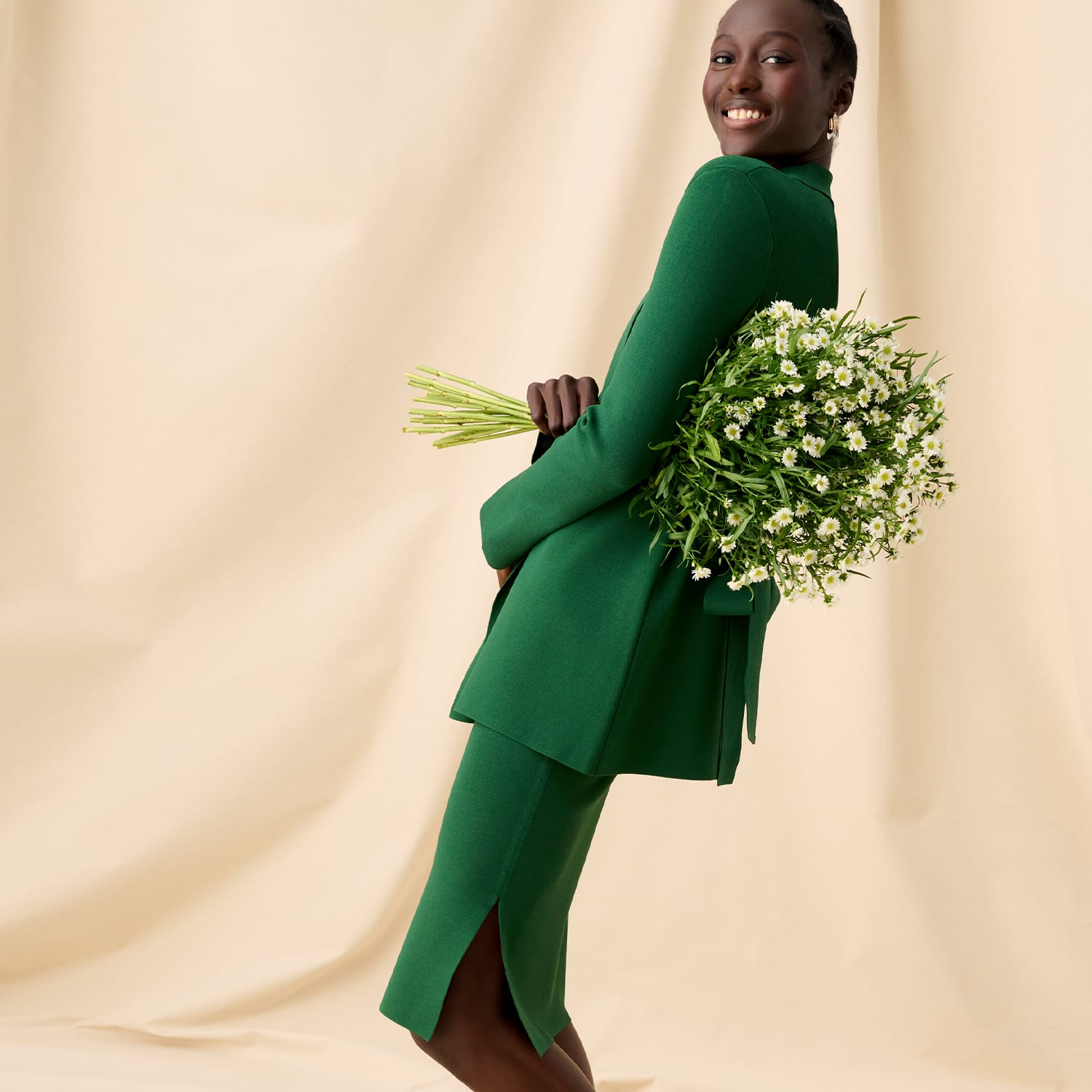 Image of a woman wearing the merrit jardigan in vine and harlem skirt in vine holding a bouquet of flowers