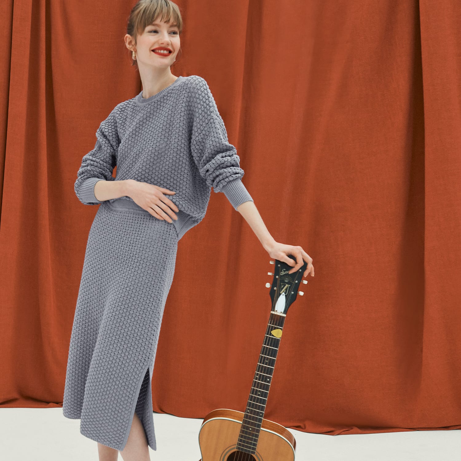 Woman in liam sweater and senga skirt leaning on a guitar