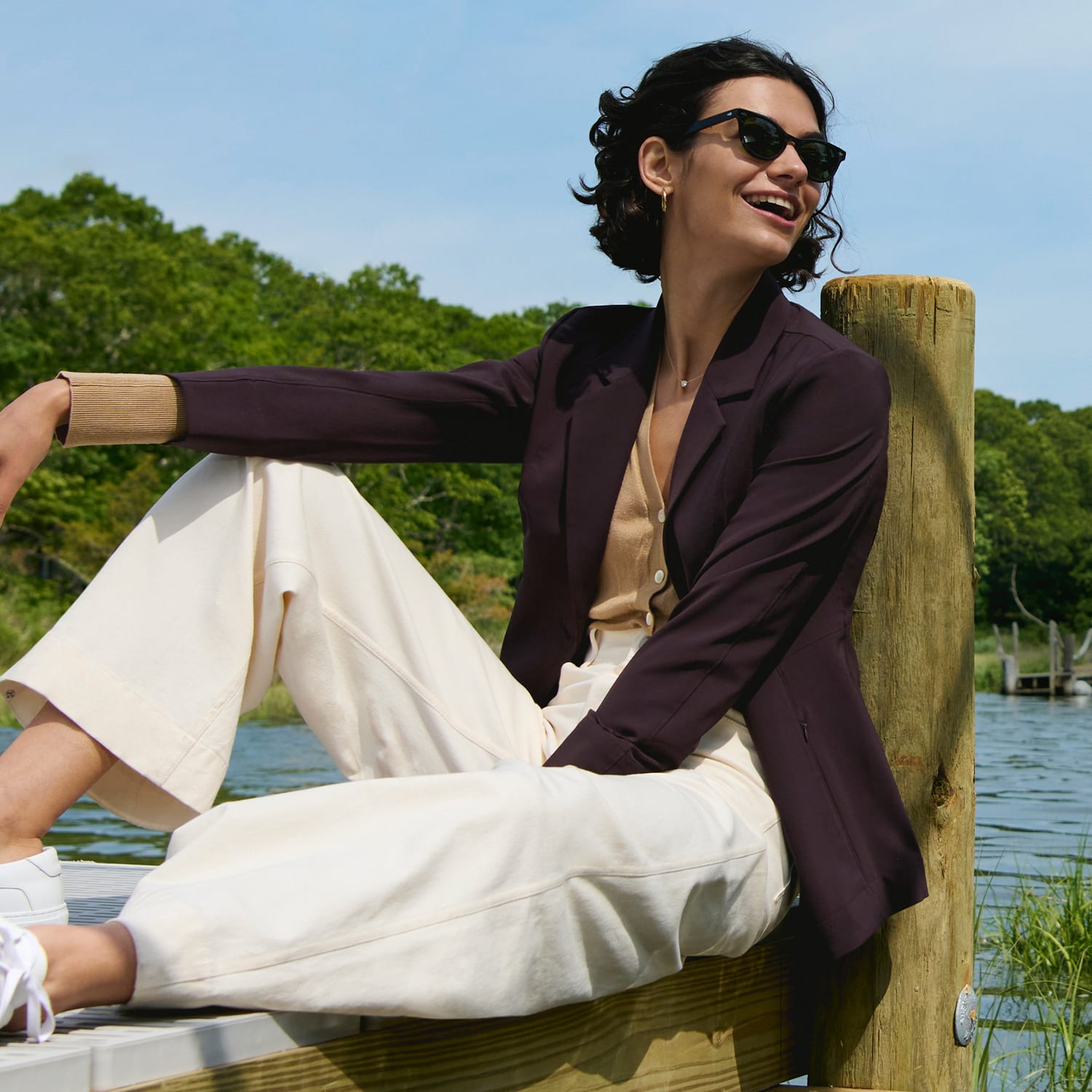 image of a woman sitting on a dock wearing a wine colored blazer with a camel colored top and ivory pants