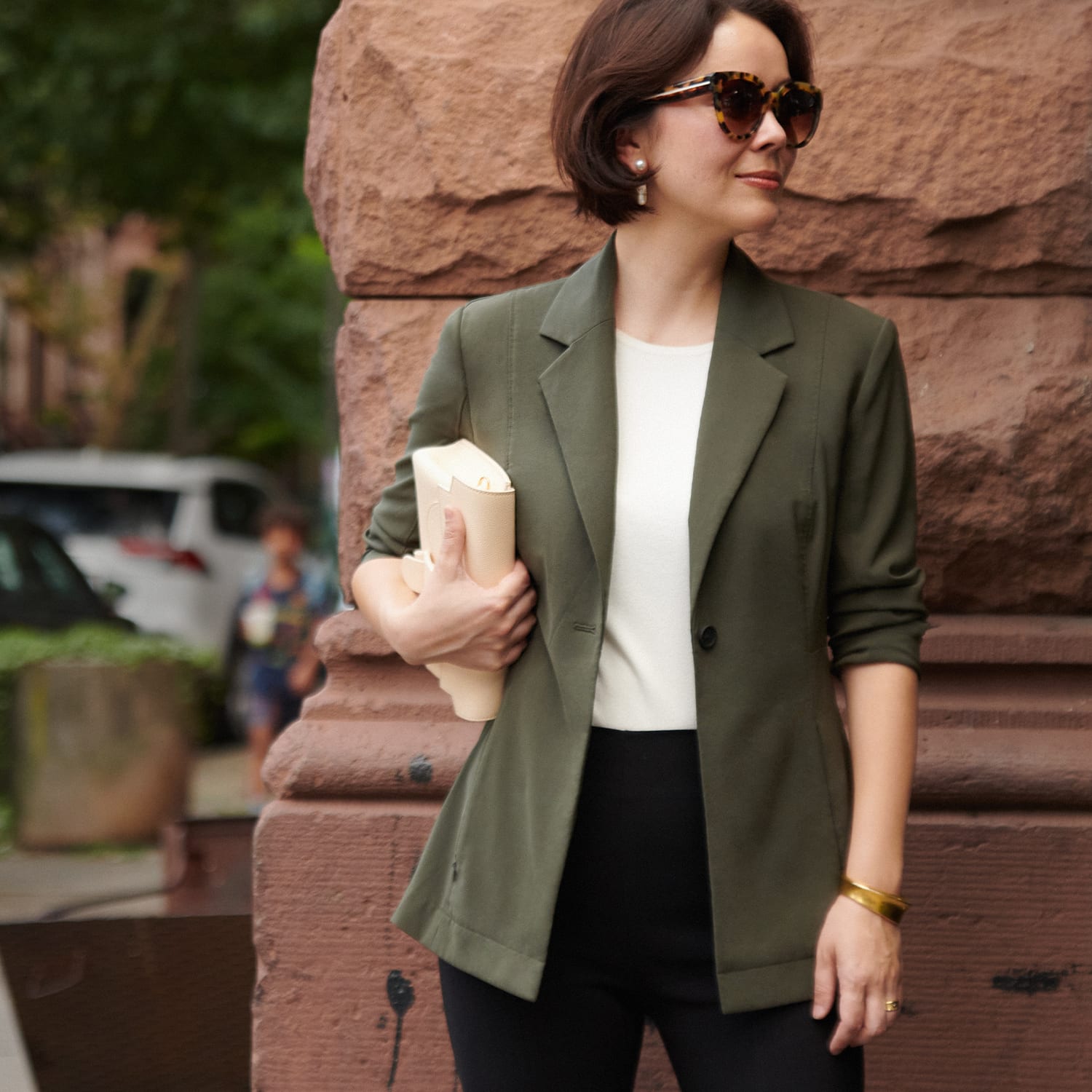 image of Sarah LaFleur standing on the street wearing an olive jacket with a white top and black pants