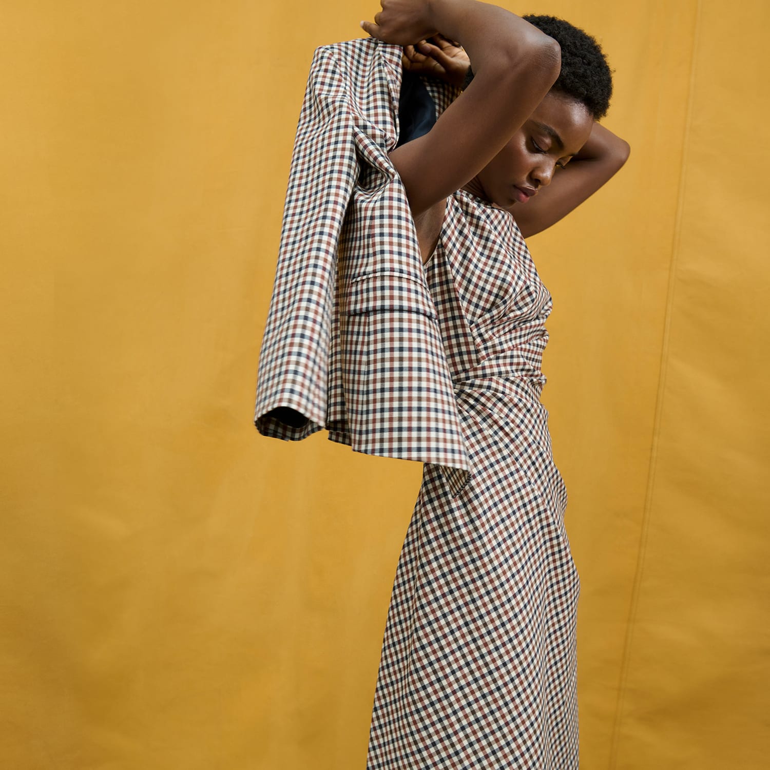 image of a woman in front of a yellow back drop wearing a plaid suit