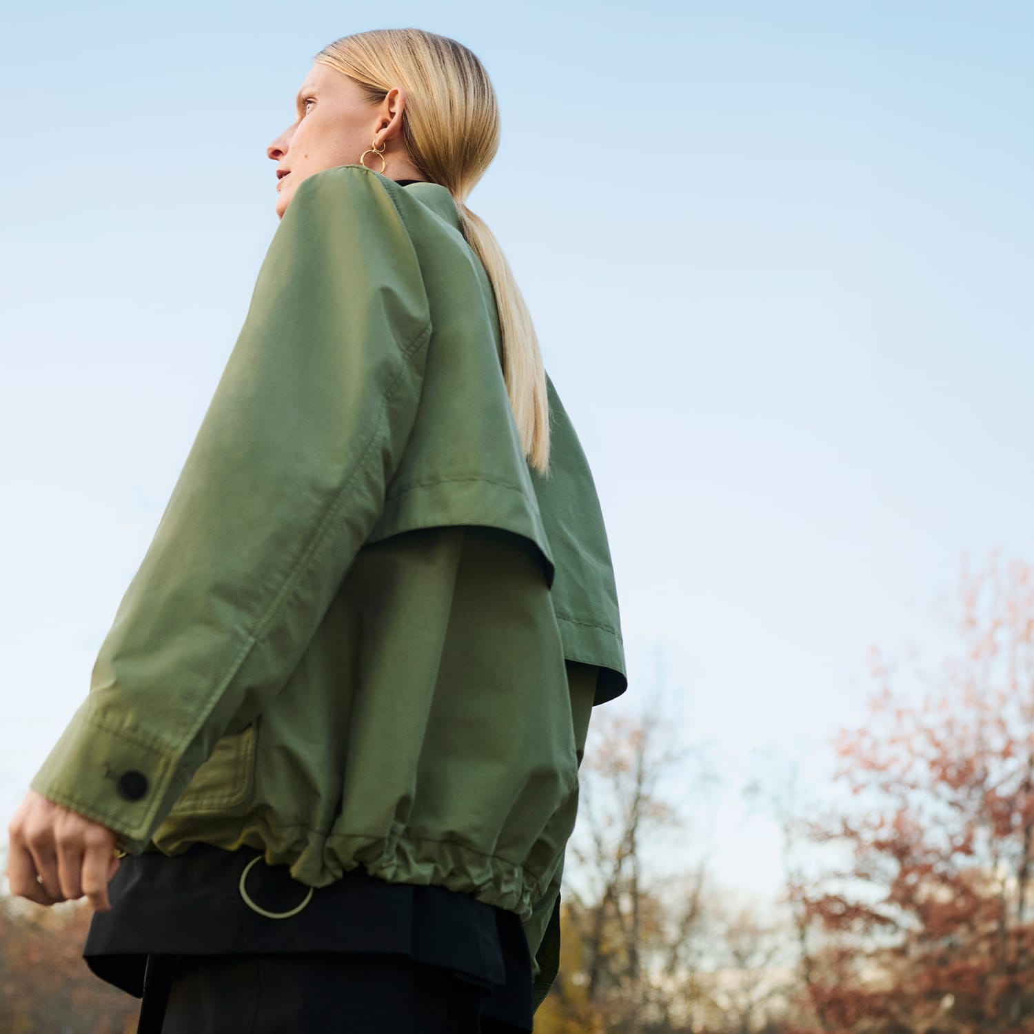 woman with blond ponytail with her back to camera looking into distance, wearing green outerwear jacket