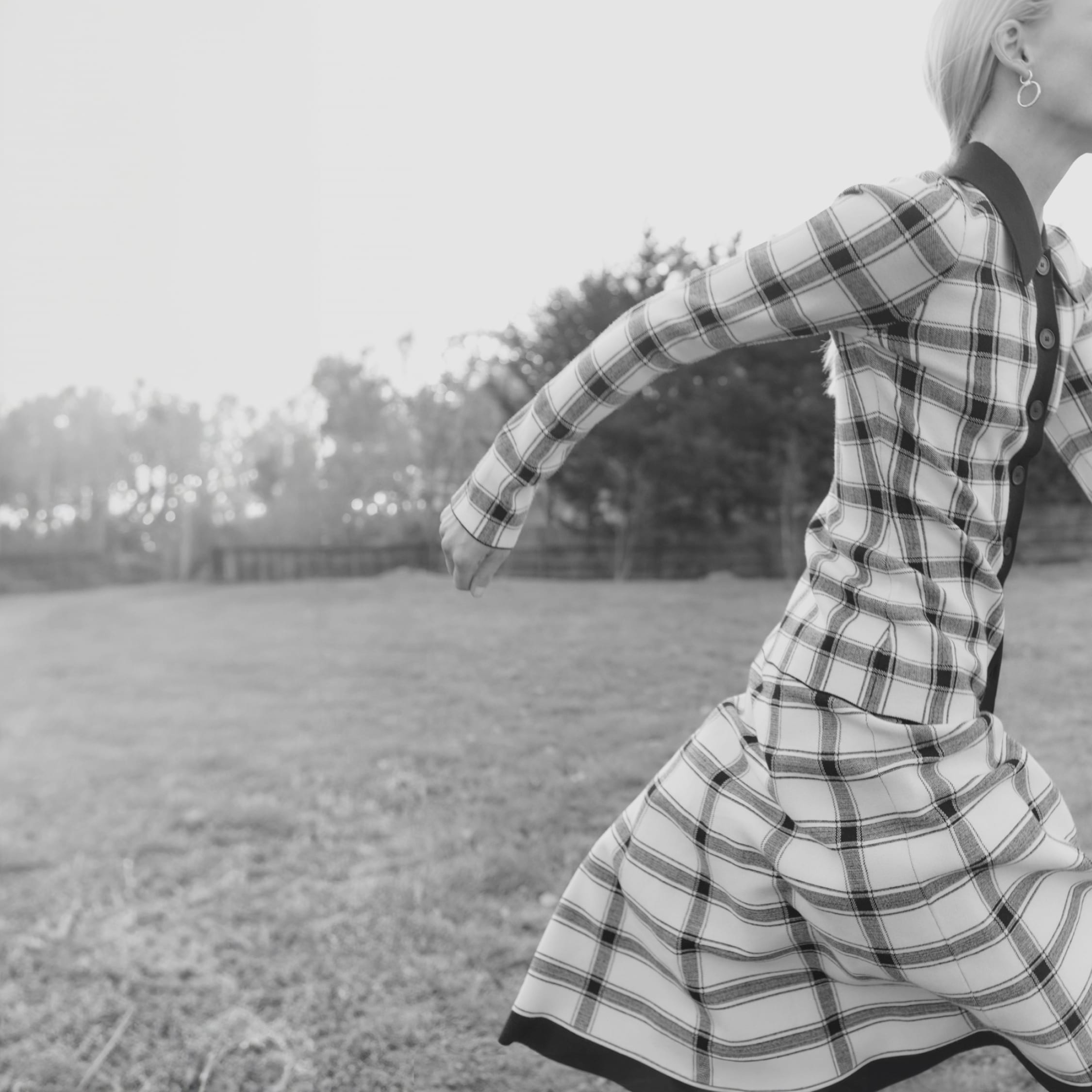 black and white image of woman wearing plaid knit top + skirt set, running off the side of the image