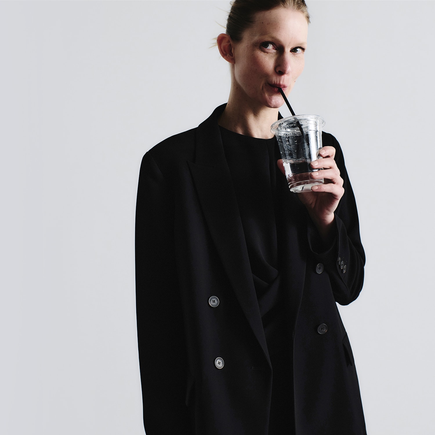 woman wearing black blazer and sipping water from clear cup