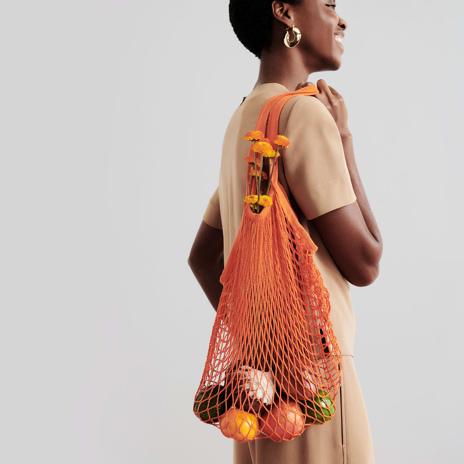 image of a woman wearing the annika top and elena culotte in light saddle holding a mesh bag of fruit