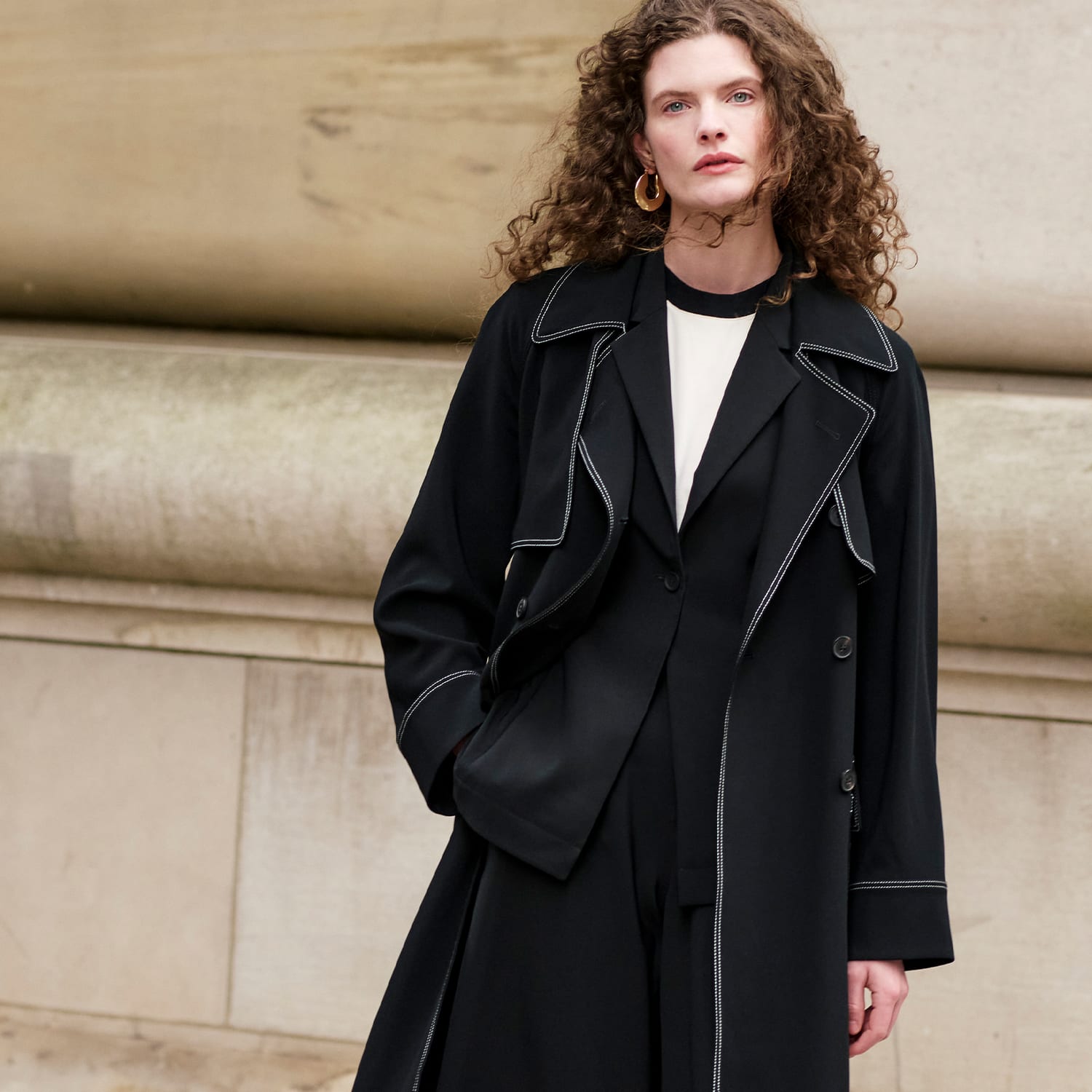 image of a woman wearing a black trench coat standing by a building