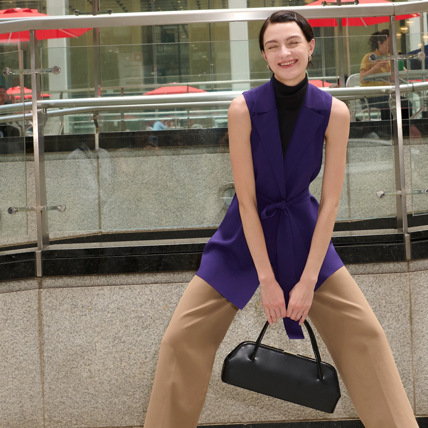 woman standing wearing the jett turtleneck tank in black, anh jardigan vest in amethyst and the milo jean in saddle