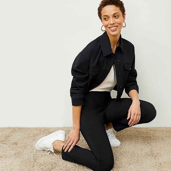 woman kneeling in jacket, cigarette pants, and sneakers