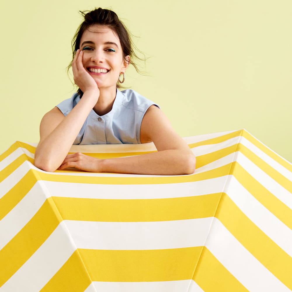 woman standing behind a yellow and white striped umbrella