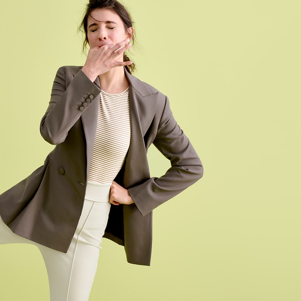 Woman in mink colored jacket, striped shirt and white pants on a green background