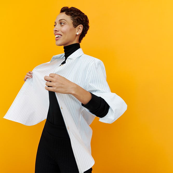 woman standing wearing a white button down over a black turtleneck on a yellow backdrop