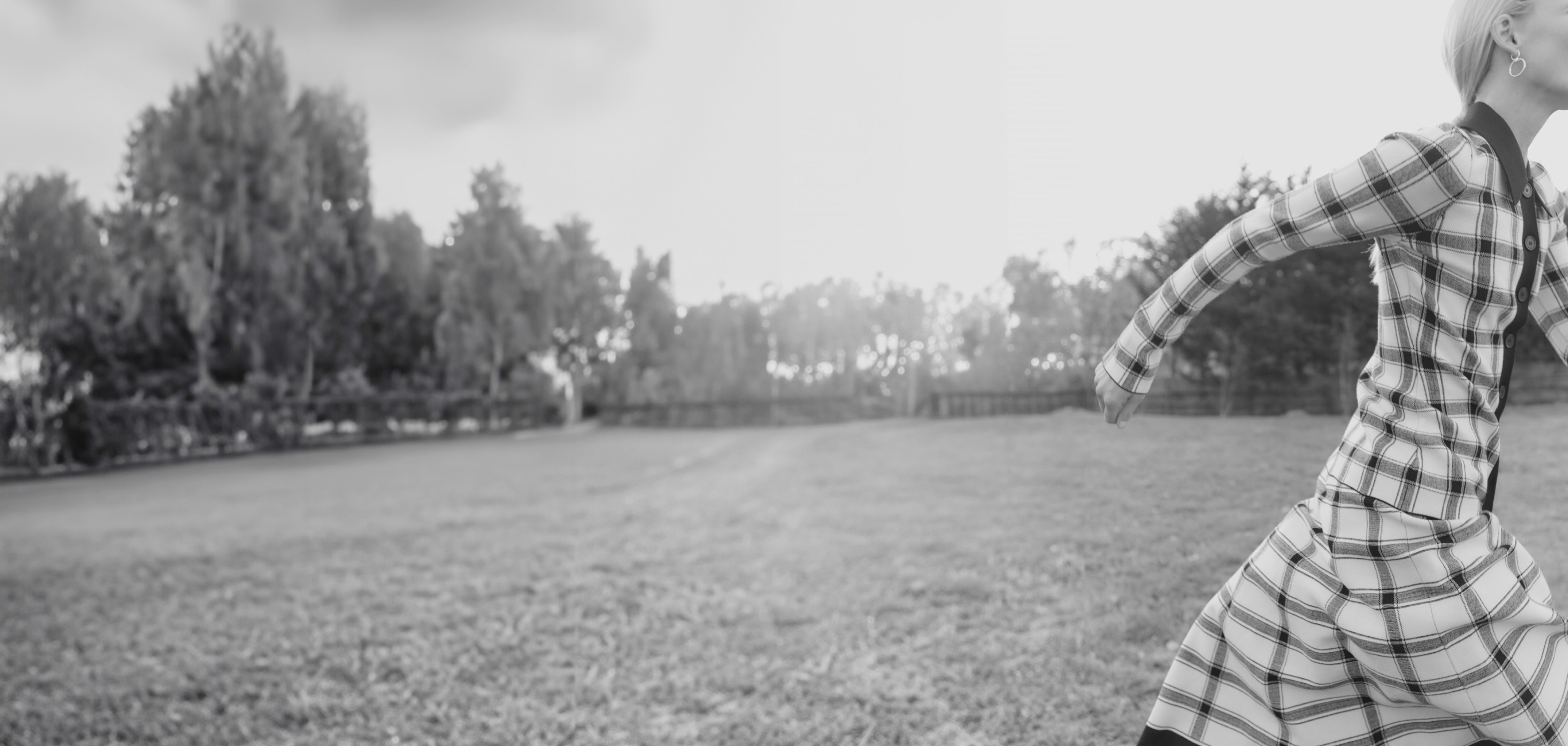 black and white image of woman wearing plaid knit top + skirt set, running off the side of the image