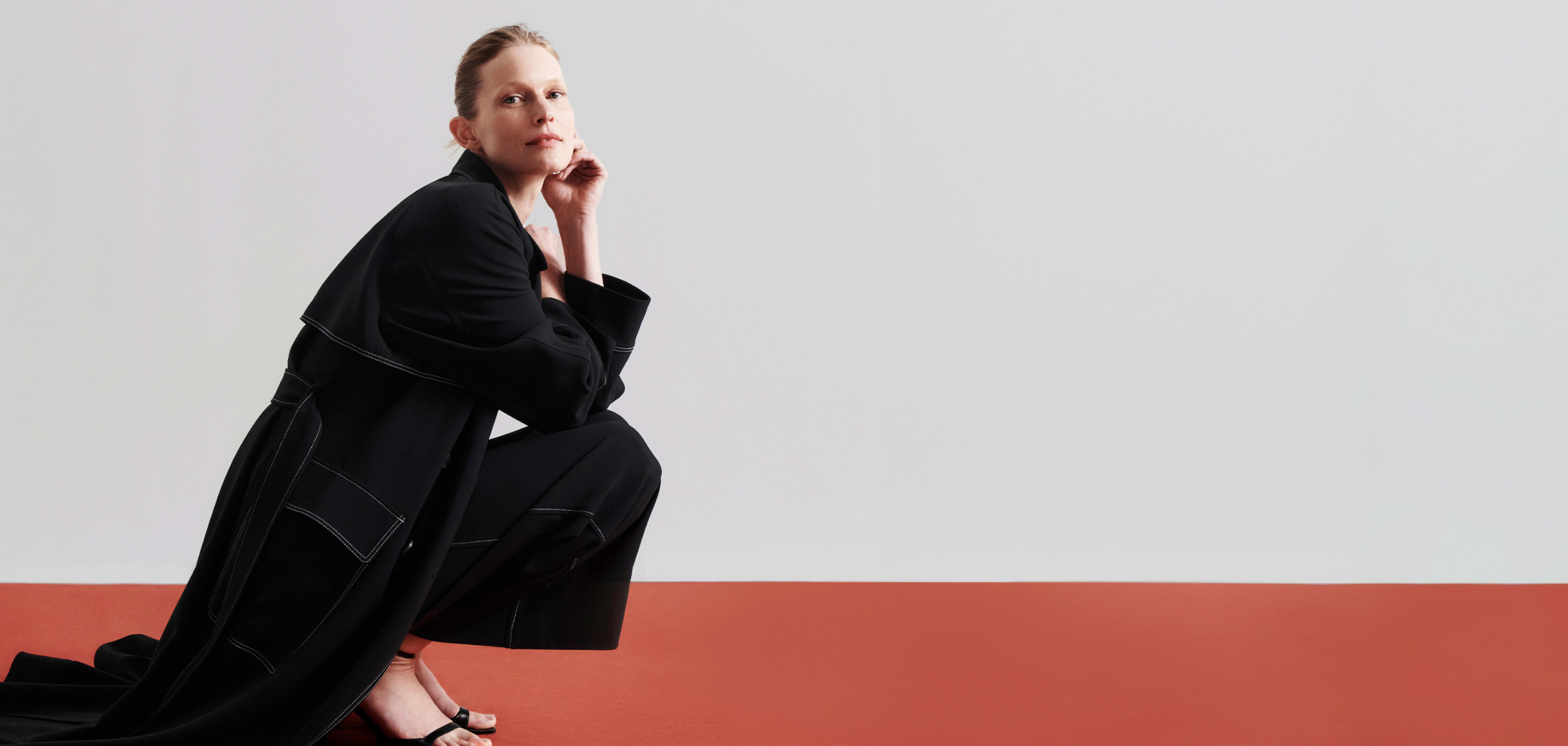 woman wearing black Trench coat crouching down on red floor