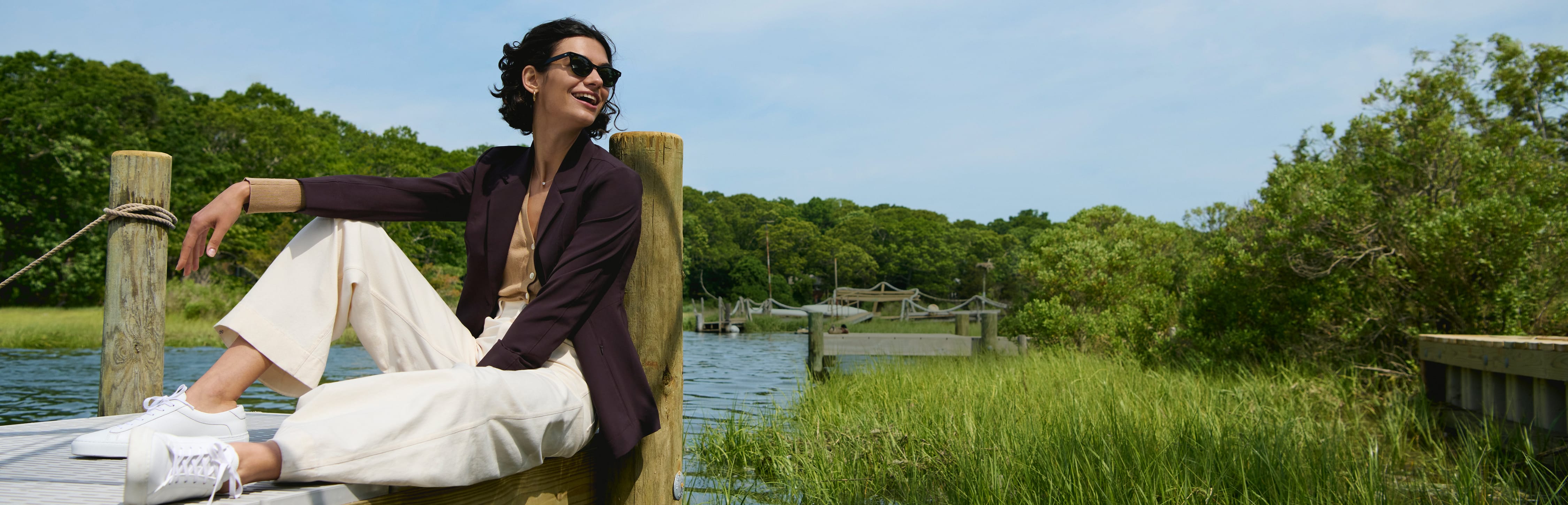 image of a woman sitting on a dock wearing a wine colored blazer with a camel colored top and ivory pants