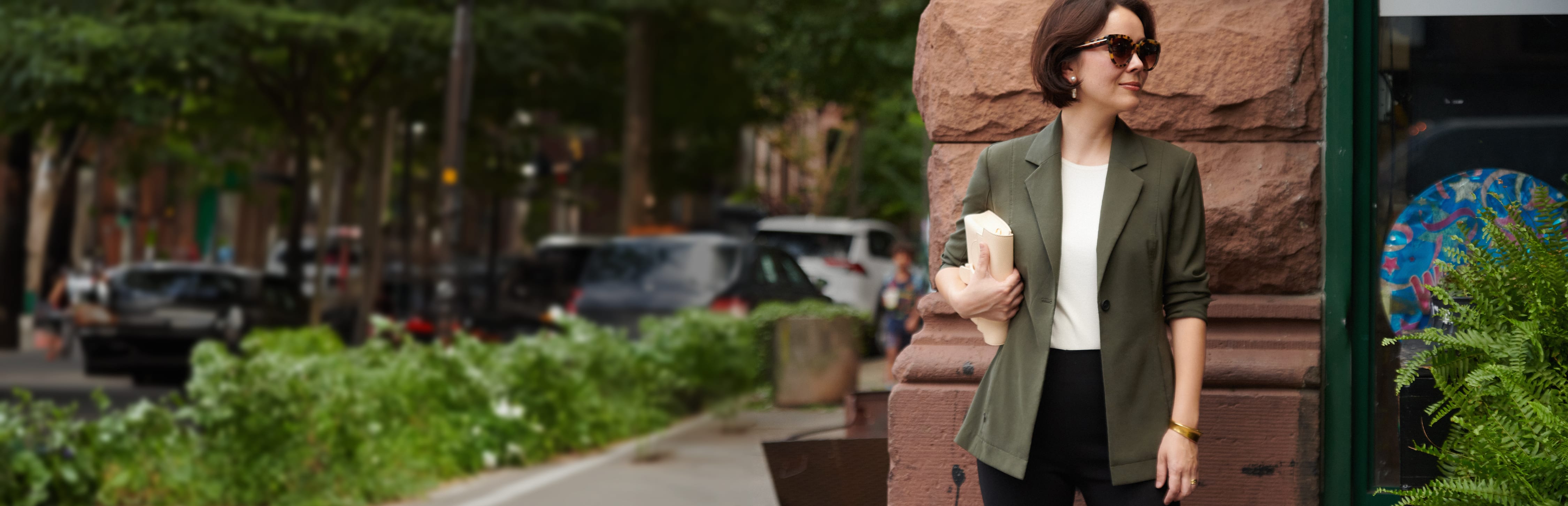 image of Sarah LaFleur standing on the street wearing an olive jacket with a white top and black pants