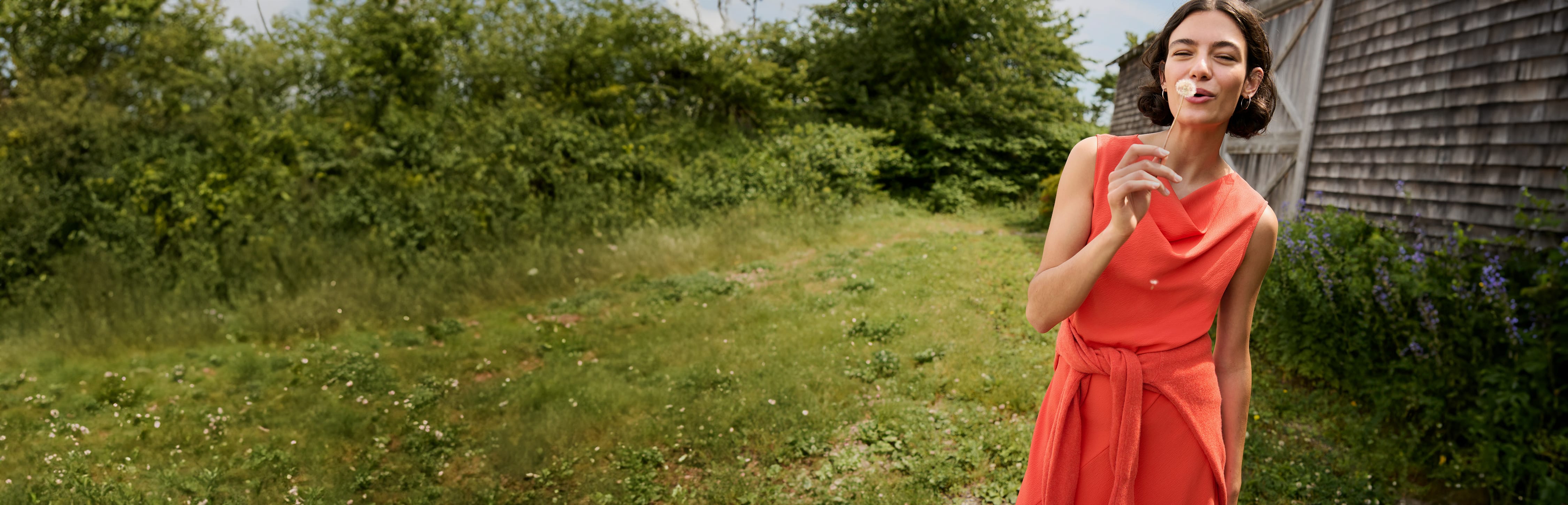 image of a woman wearing the priya dress in bright coral