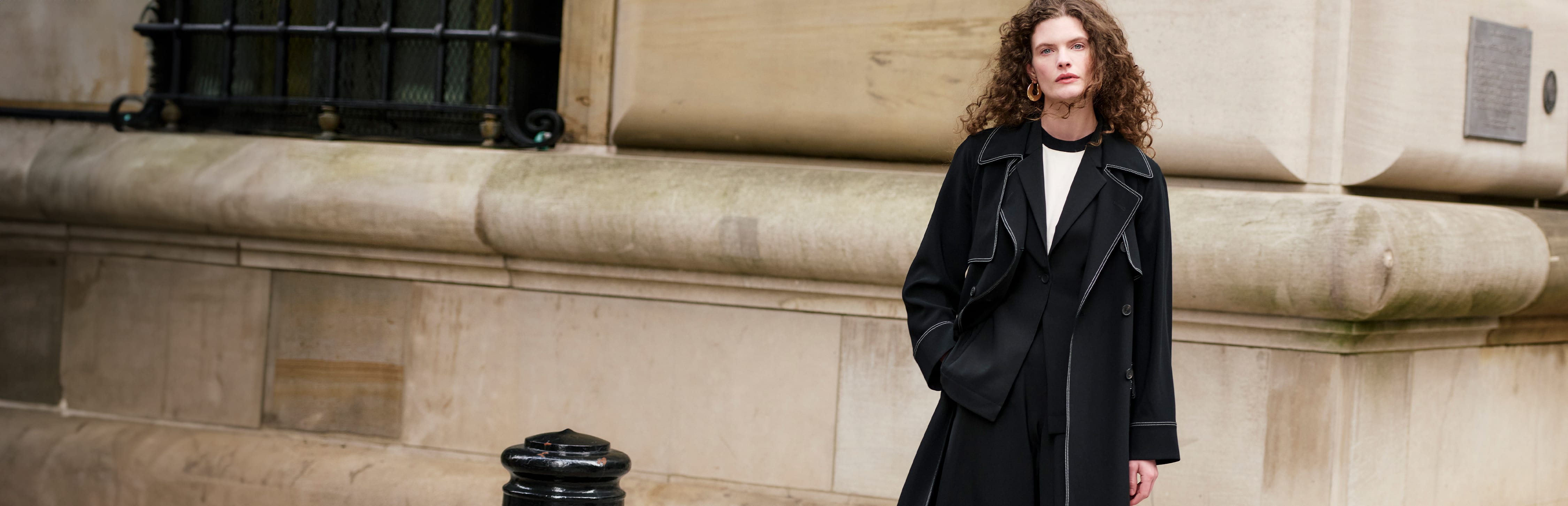 image of a woman wearing a black trench coat standing by a building