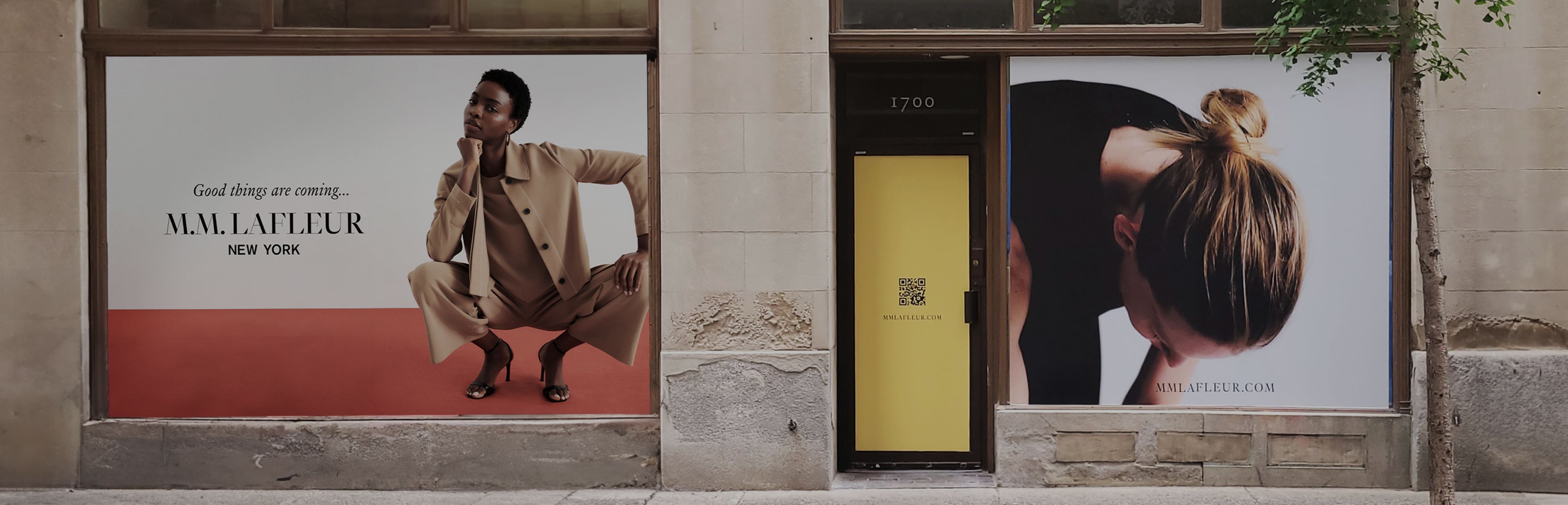 Exterior of upcoming M.M.LaFleur Philadelphia store: tan brick wall with two large windows covered with images that say M.M.LaFleur (Good Things Are Coming)