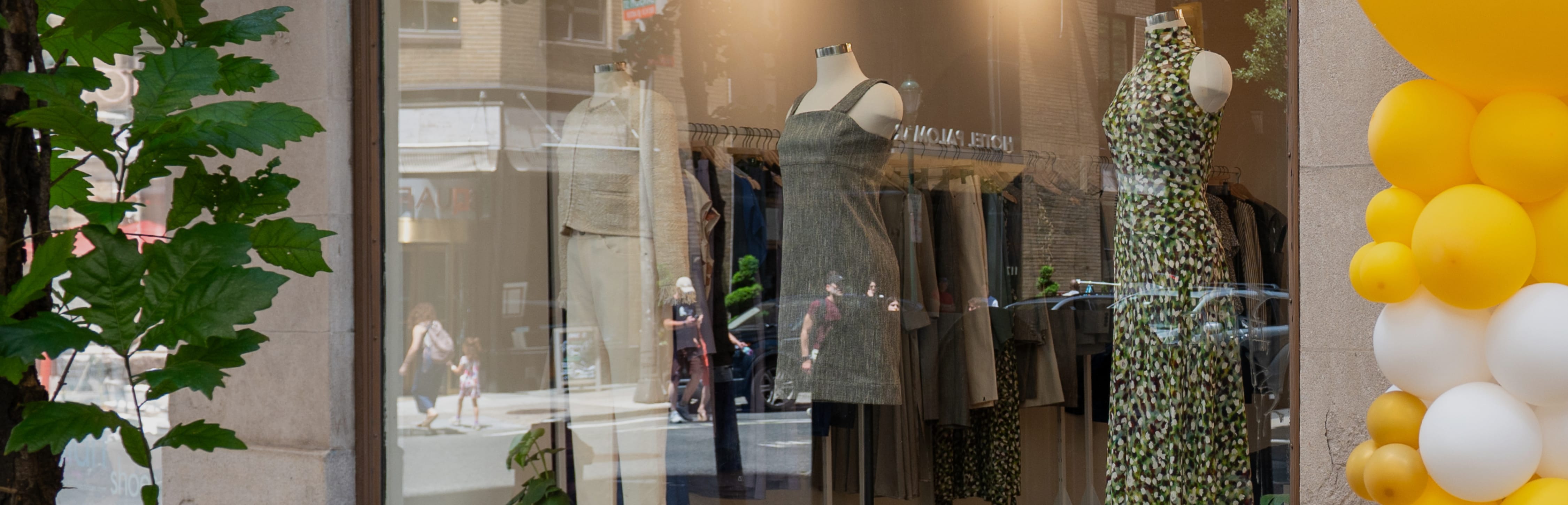 Exterior of M.M.LaFleur Philadelphia store: mannequins in a window dressed in a green sleeveless dress, gray dress, and white cardigan with white jeans