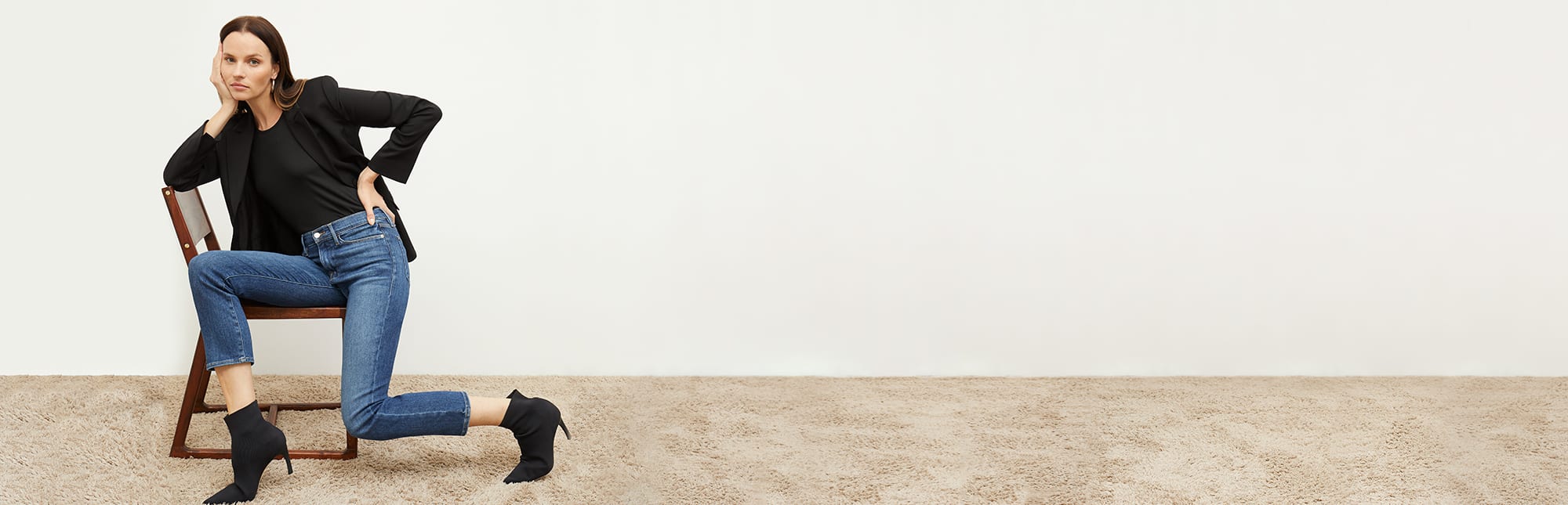 woman sitting on a chair wearing the black yiyan blazer, a black t shirt, frame jeans and the black lana boots