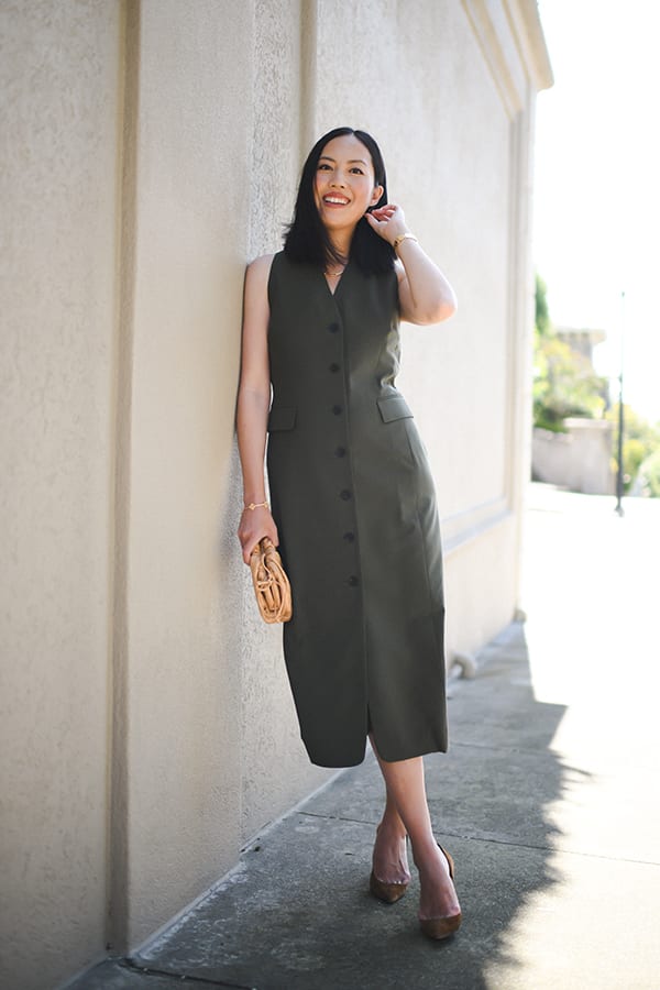 woman leaning against a wall wearing the cassandra dress in olive with cognac colored shoes