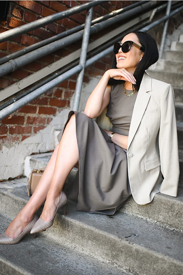 woman sitting on stairs wearing the jeannine dress in mink with the yiyan blazer in natural melange draped over her shoulders and the ginger pump in rosy type