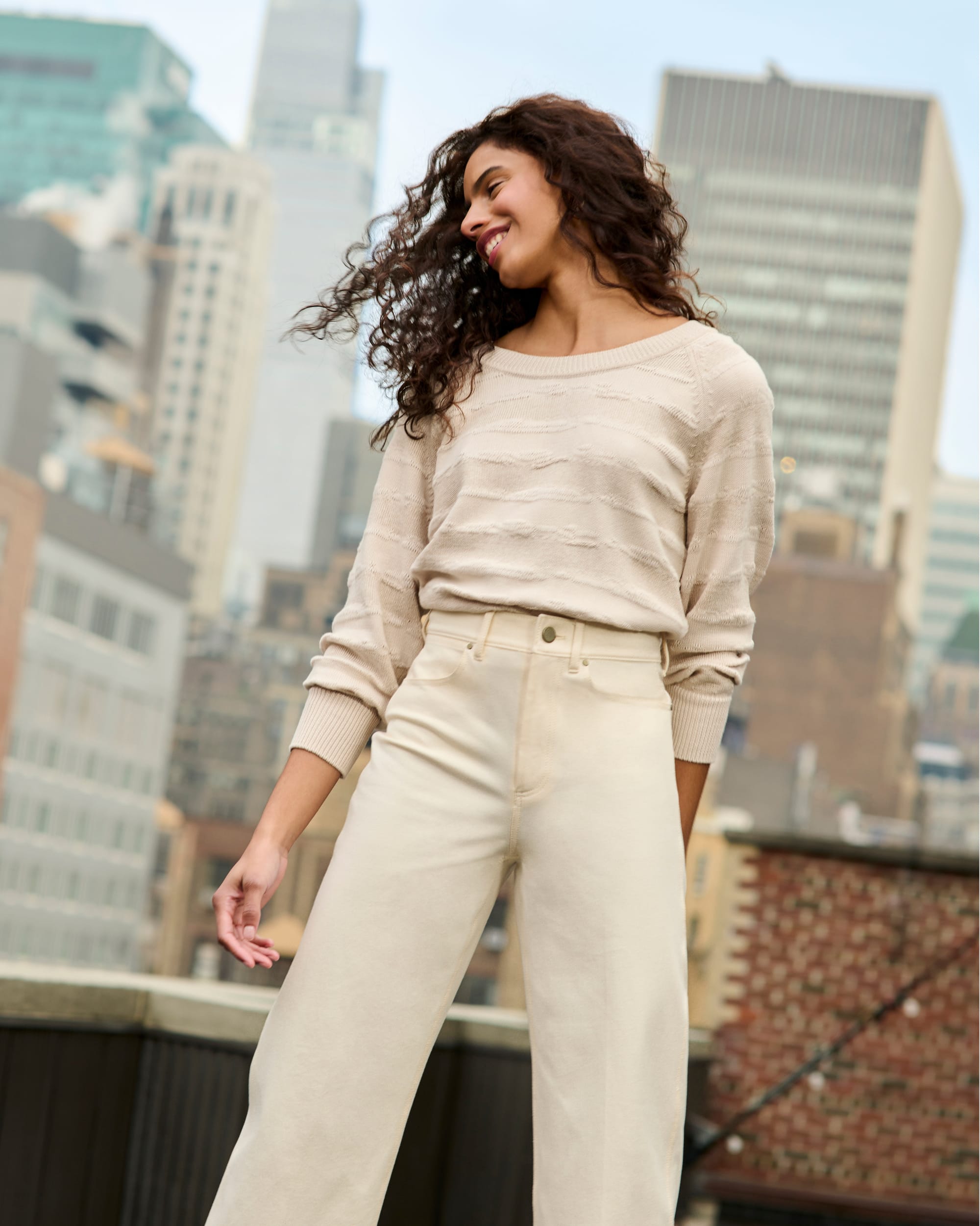 image of a woman standing wearing the jo sweater and milo jeans in front of a skyline