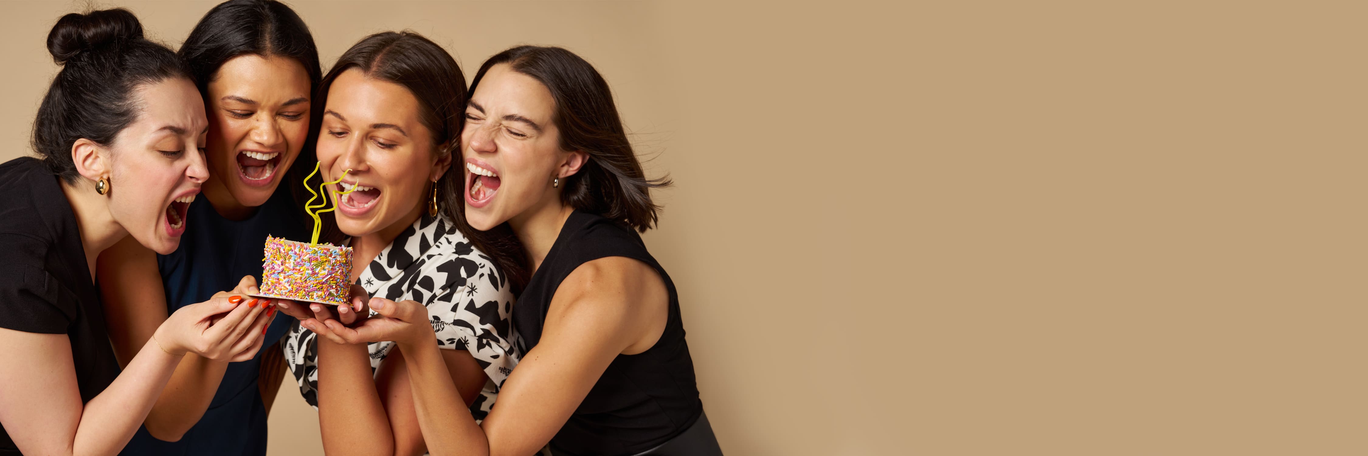 image of four women taking a bit into a cake while wearing the M.M. LaFleur Heritage Dresses