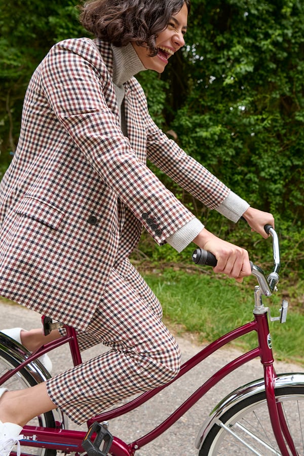 image of a woman riding a bike while wearing the mejia pant in windowpane multi and the ohara jacket in windowpane multi
