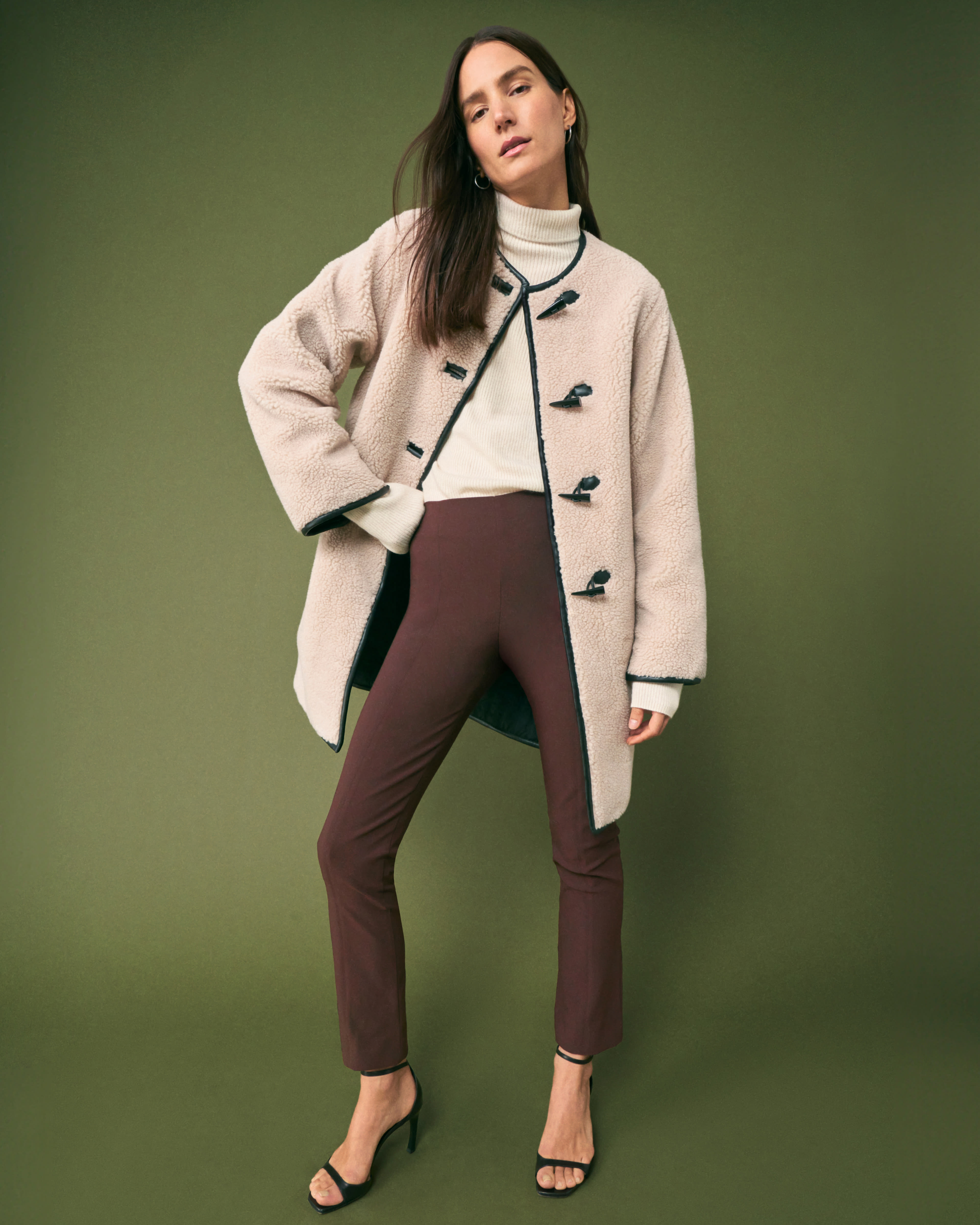 front image of a woman standing wearing the katari jacket with the mckenzie sweater in cream and the foster pants in mahogany