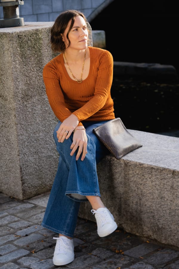 image of a woman sitting wearing the rae top in caramel wearing the frame jean in drizzle