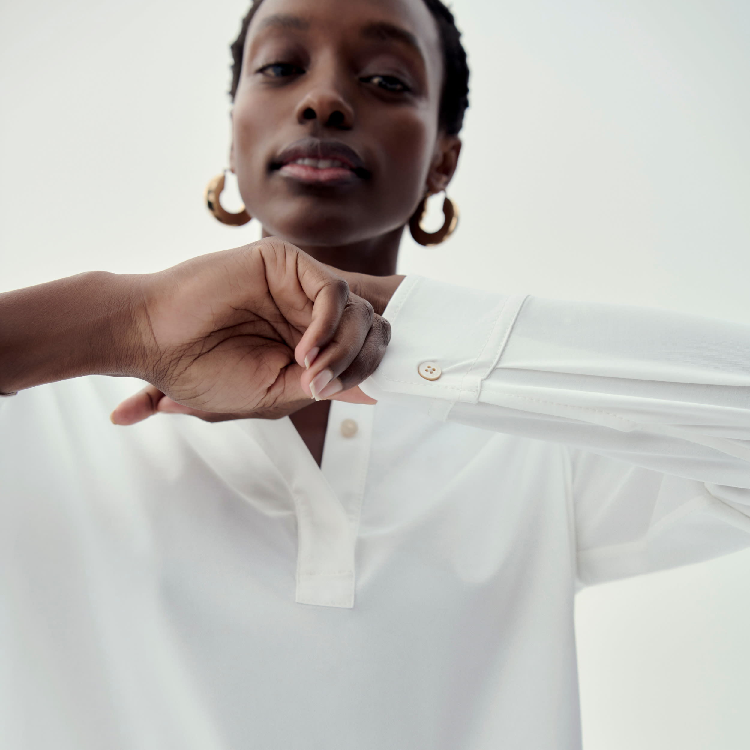 close-up image of woman wearing white long-sleeve top, holding one sleeve in front of her